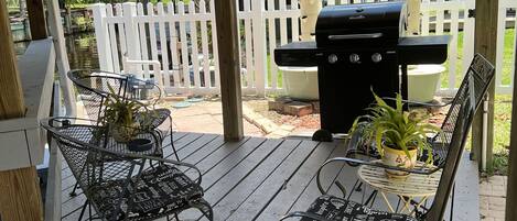 A covered patio with a grill, metal chairs, and a table.