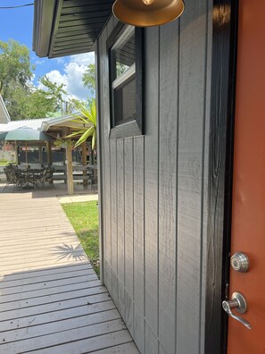 Une porte en bois avec une poignée en métal, une fenêtre et une vue sur un patio extérieur aménagé avec une table et des chaises.