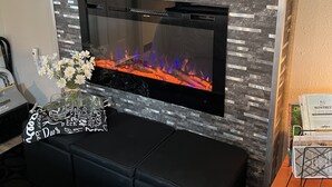 Een moderne woonkamer met een open haard, een flatscreen televisie erboven en een houten plank met diverse spullen.