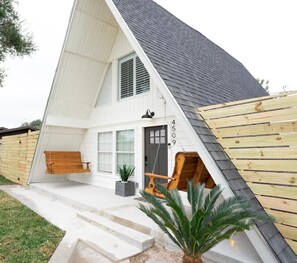 A modern A-frame house with a front porch, a swing chair, and a small garden area. - A pet friendly A-Frame with a hot tub & fire pit! (McAllen)
