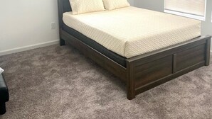 Une chambre à coucher avec un lit en bois foncé, une fenêtre avec des stores et un sol recouvert de moquette.