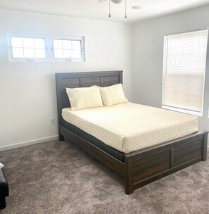 A bedroom with a dark wooden bed, a window with blinds, and a carpeted floor.
