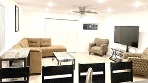 Un salon comprenant un canapé, des fauteuils, une table basse, un téléviseur et un ventilateur de plafond.