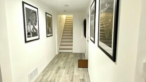 Un couloir doté d’un parquet en bois clair, de murs blancs et de tableaux encadrés accrochés aux murs.