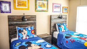 Ein Hotelzimmer mit zwei Betten, jeweils mit Mickey Mouse-Motiven. An den Wänden befinden sich gerahmte Disney-Bilder und ein hölzernes Kopfende.