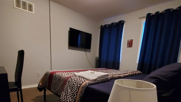 Habitación de hotel con cama, televisor montado en la pared, escritorio con lámpara y una silla.