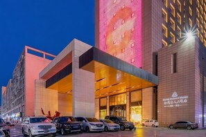 Un hotel modern amb una entrada destacada, un aparcament amb diversos cotxes i una façana ben il·luminada.