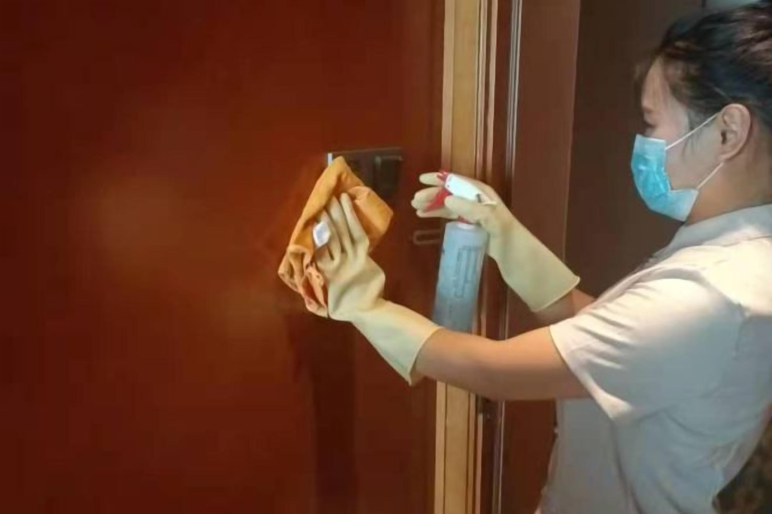 A person cleaning a door with a cloth and spray bottle.