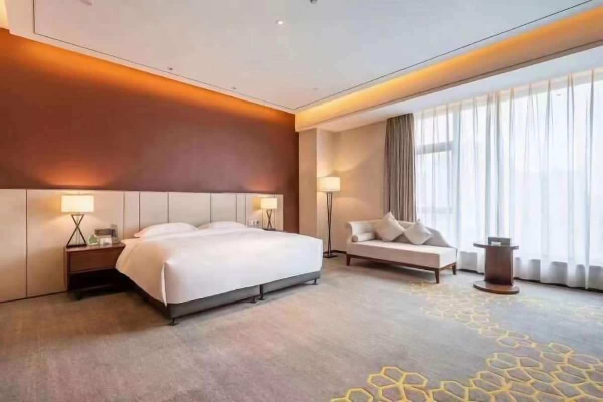 A hotel room with a large bed, a sofa, a nightstand, and a lamp.