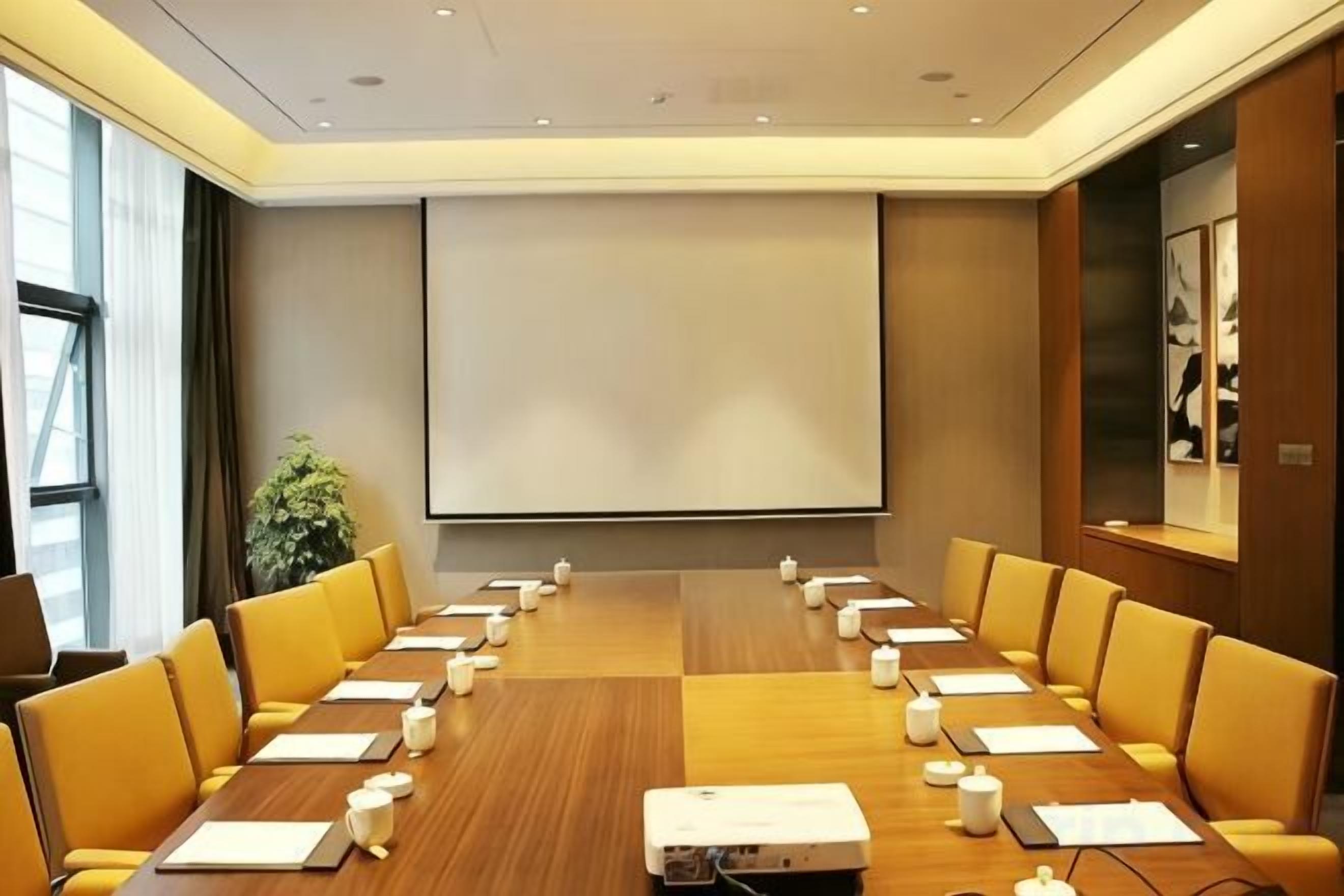 A conference room with a long table, chairs, a projector, and a screen.