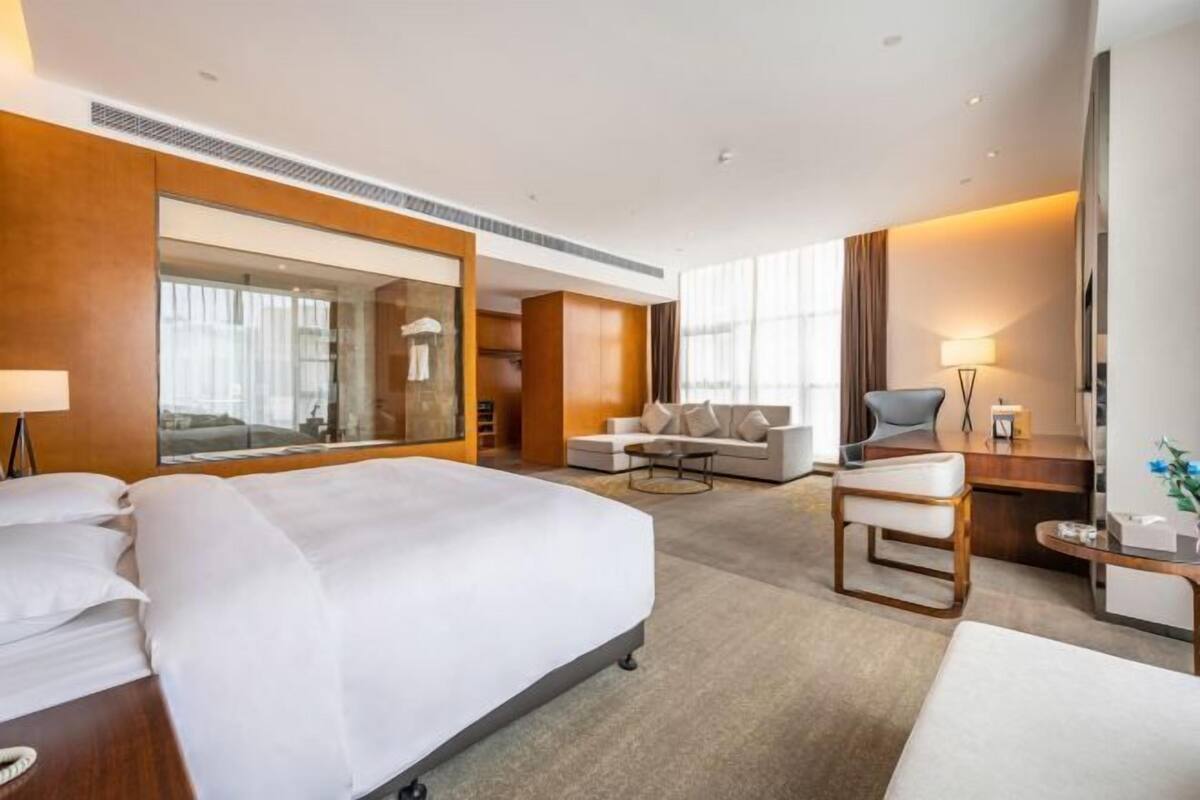 A modern hotel room with a large bed, a sofa, a desk, and a large mirror.