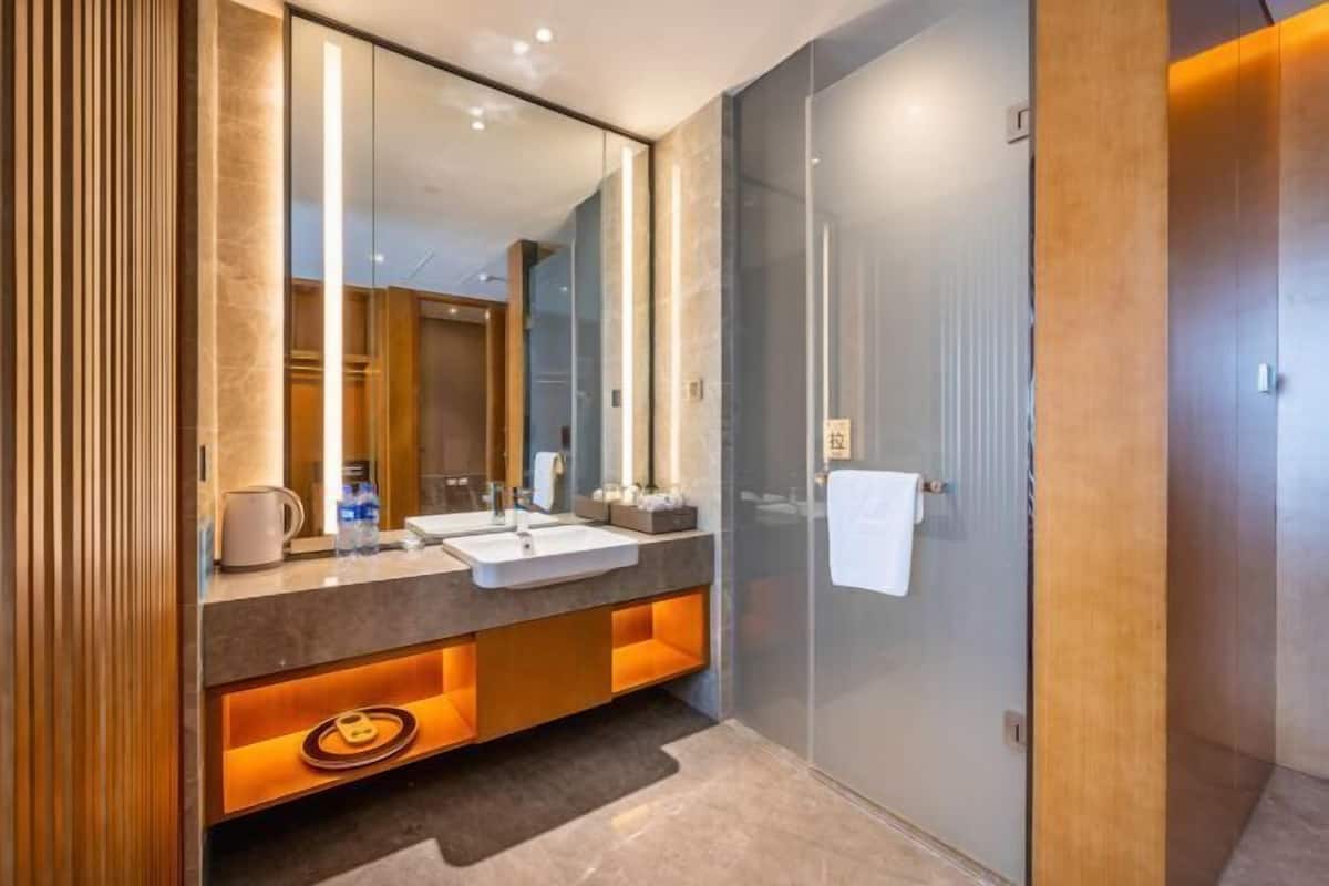 A modern bathroom with a large mirror, two sinks, and a walk-in shower.
