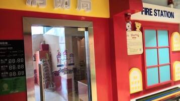 A fire station entrance with a yellow sign, a digital clock displaying 88:88, and a colorful interior with a bench and a toy train.
