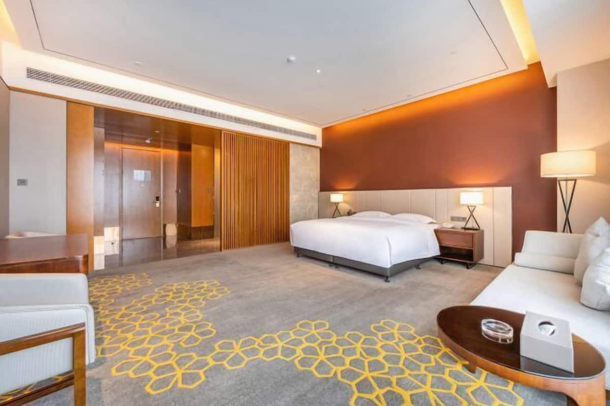 A modern hotel room with a large bed, a sofa, a desk, and a bathroom.