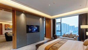 Habitación de hotel moderna con una cama grande, un televisor de pantalla plana en la pared y vistas a la ciudad a través de amplios ventanales.