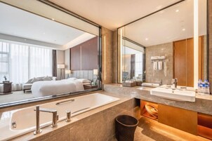A modern hotel bathroom with a large mirror, a bathtub, and a vanity with a sink and mirror.