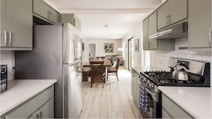 Une cuisine moderne avec des meubles gris, un réfrigérateur en acier inoxydable, une cuisinière à gaz et un coin repas comprenant une table et des chaises.