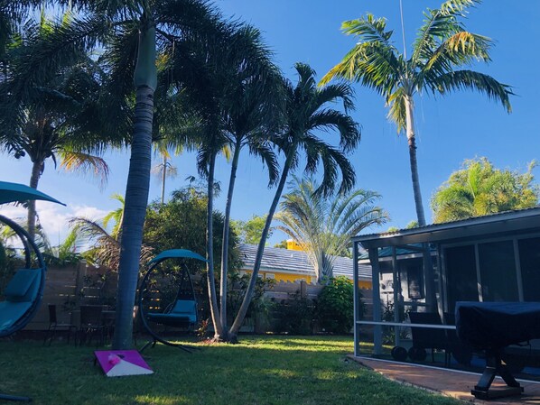 A backyard with a swing set, a covered seating area, and a barbecue grill.