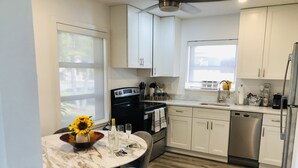 Une cuisine moderne avec des meubles blancs, une cuisinière noire, des appareils en acier inoxydable et une table à manger agrémentée d’un vase de tournesols.