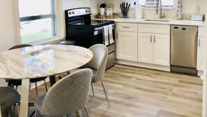 Une cuisine moderne avec des meubles blancs, une cuisinière noire, une table en marbre et un ventilateur de plafond.