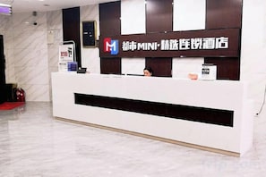 Una recepción con un cartel que indica que es un hotel 'MINI', un extintor y un reloj digital.