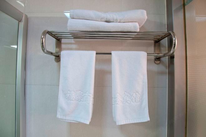 A bathroom with a glass shower door, a metal towel rack with two folded towels, and a folded towel on top.