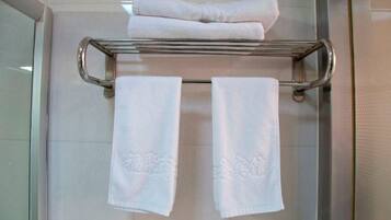 A bathroom with a glass shower door, a metal towel rack with two folded towels, and a folded towel on top.