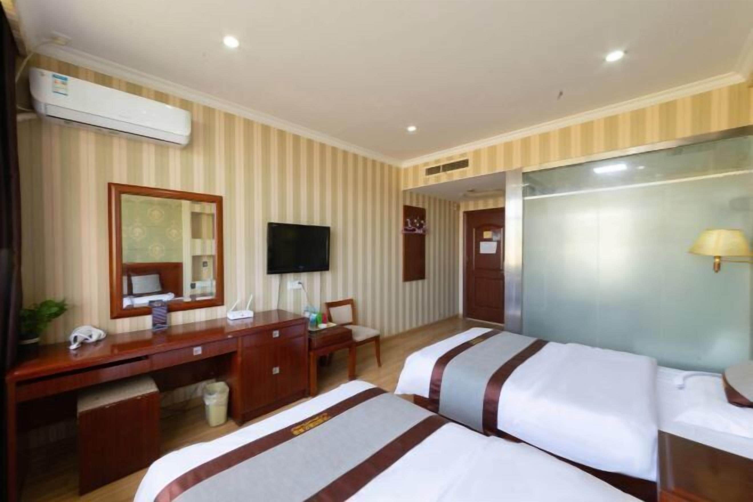 Una habitación de hotel con dos camas, un escritorio, un televisor y un espejo.