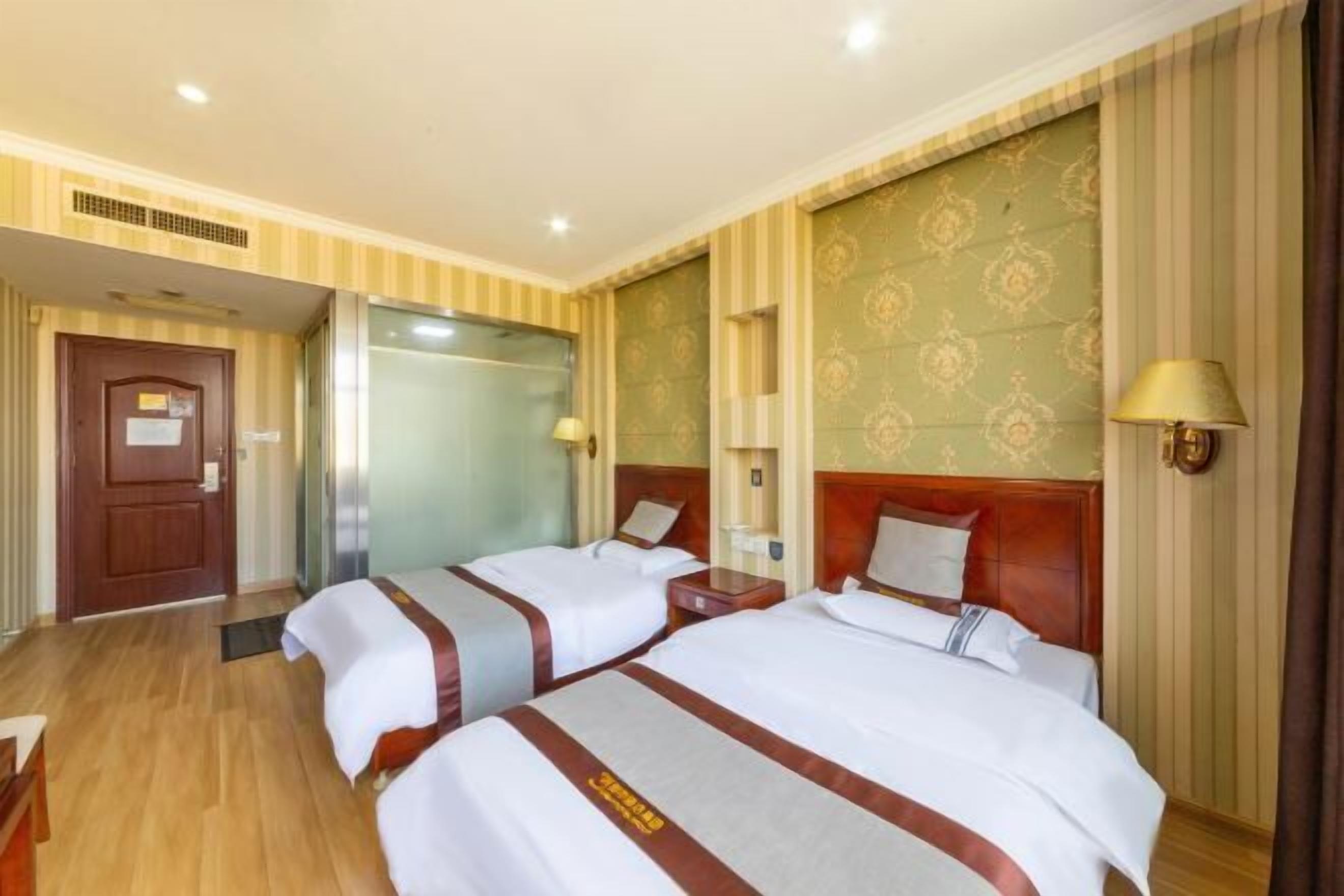 Una habitación de hotel con dos camas, suelo de madera, pared estampada y una puerta.