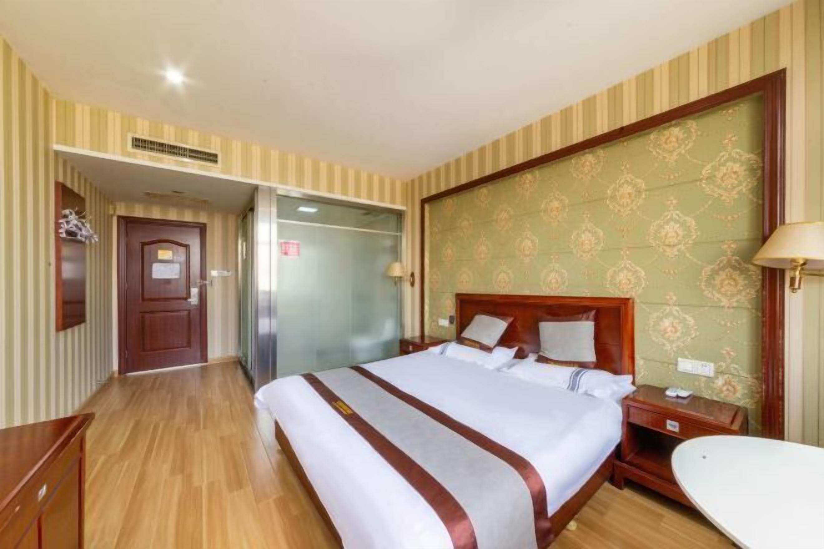 A hotel room with a large bed, wooden floor, striped wallpaper, and a patterned headboard.