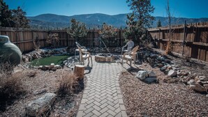 Un patio trasero con un hogar para asar, sillas exteriores y un sendero de piedra.