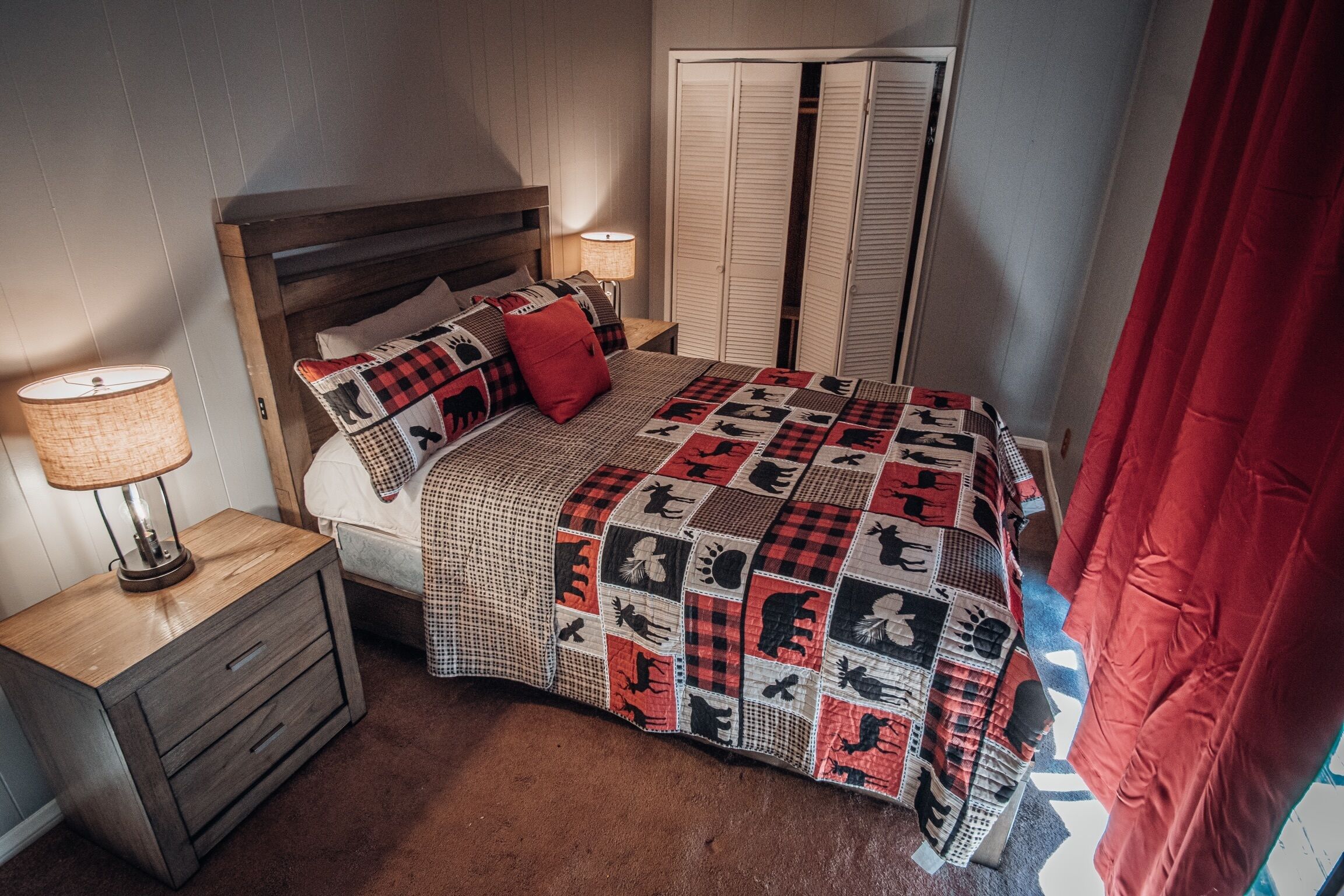 A bedroom with a bed, nightstands, a lamp, a quilt, and a closet.