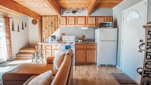 Una cocina acogedora con armarios de madera, un microondas y un refrigerador. Hay un banco de madera y un taburete pequeño cerca del mostrador de la cocina.