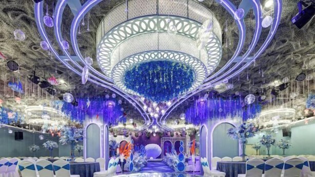 A room with a central circular platform, white chairs with blue accents, and a ceiling with hanging lights and decorations.