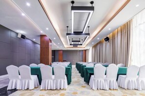 A conference room with rows of tables and chairs, a modern ceiling design, and a carpeted floor.