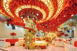 A banquet hall with a central stage, surrounded by tables with white tablecloths and red chairs.