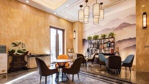 A hotel lobby with a marble floor, a round table with chairs, a bookshelf, and a large window.