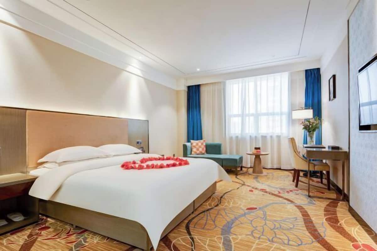 A hotel room with a large bed, a desk, a chair, and a small table.