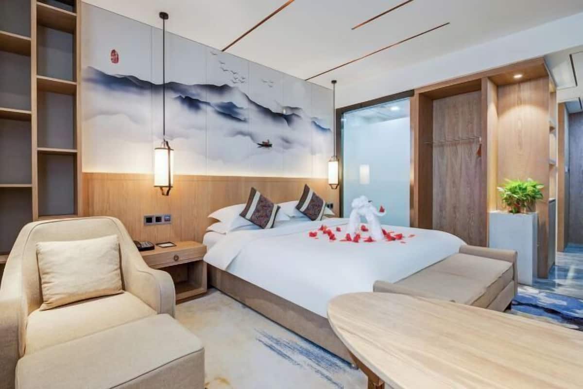 A modern hotel room with a large bed, a seating area, and a wall mural.