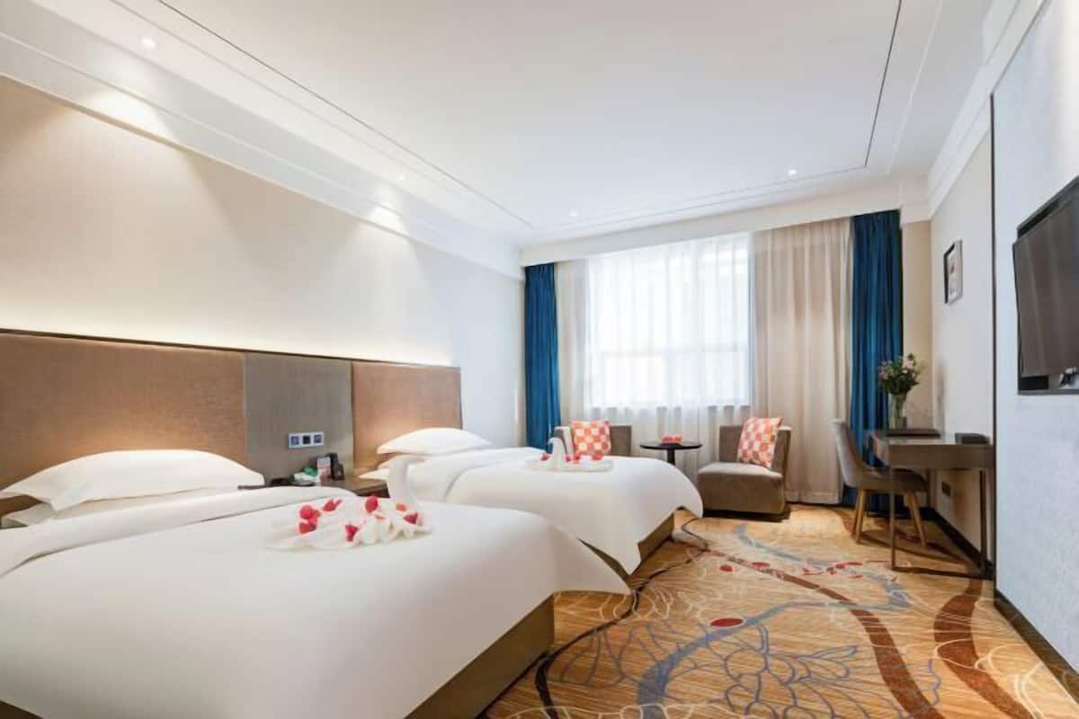 A hotel room with two beds, a sofa, a desk, and a TV.