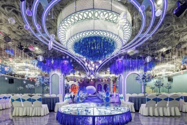 A banquet hall with a central circular table, chandeliers, and decorative elements.