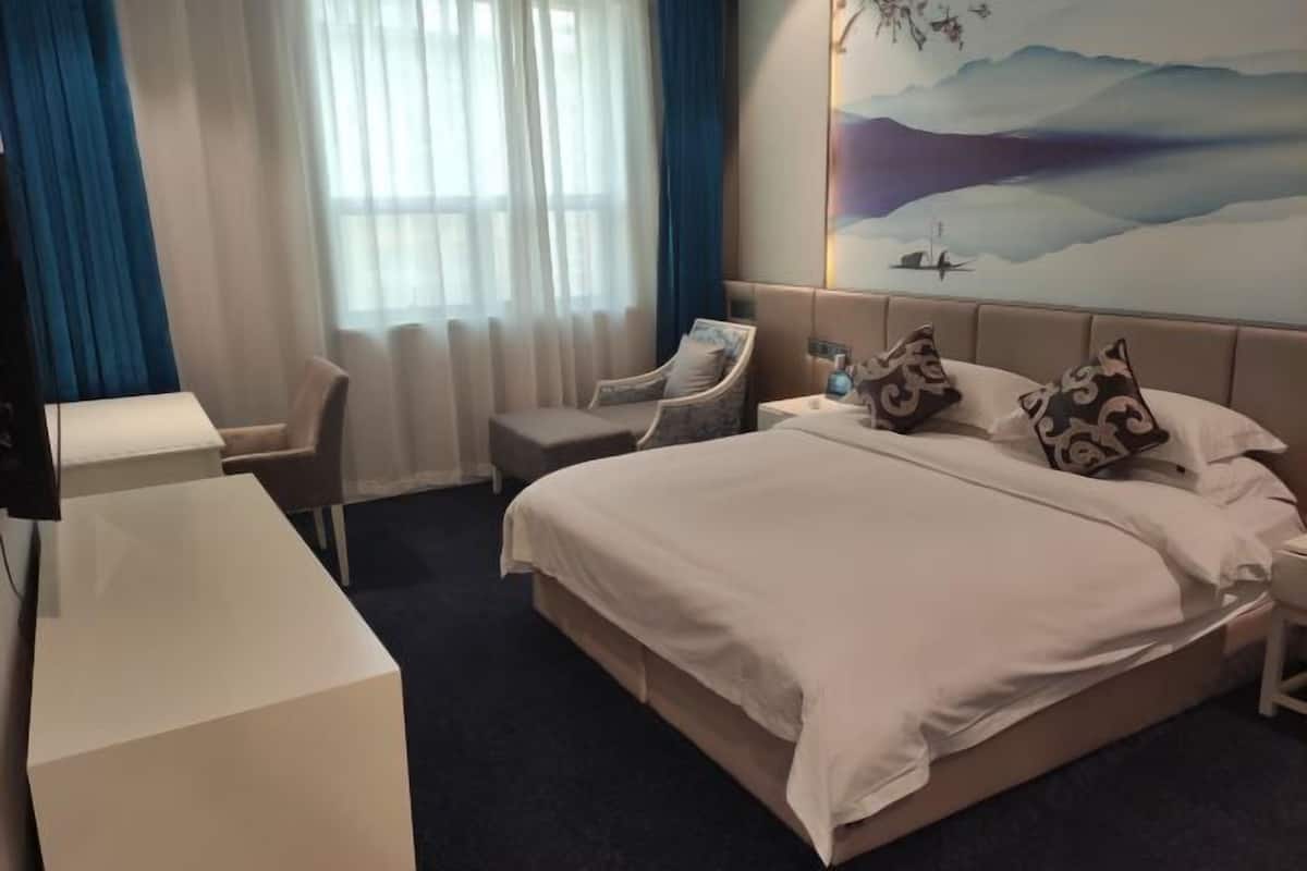 A hotel room with a bed, a desk, a chair, and a large window with curtains.