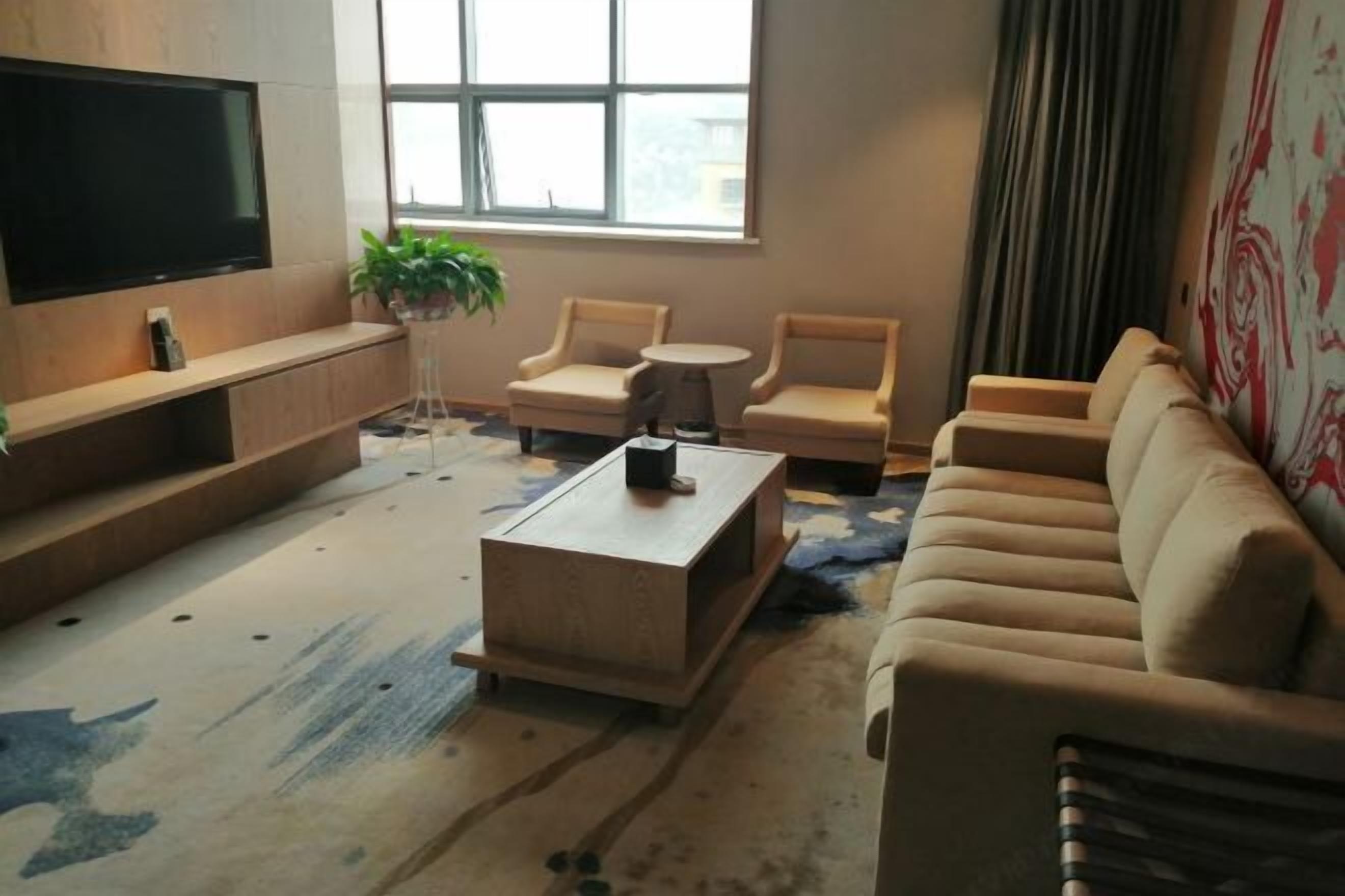 A modern living room with a flat-screen TV, beige sofas, a coffee table, and a large window with a view.