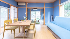 Quarto com uma mesa de jantar de madeira, cadeiras amarelas, um sofá azul e vista para o exterior através de uma porta deslizante.