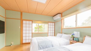 Quarto de hotel com duas camas, teto de madeira, uma janela grande e uma porta tradicional japonesa deslizante.