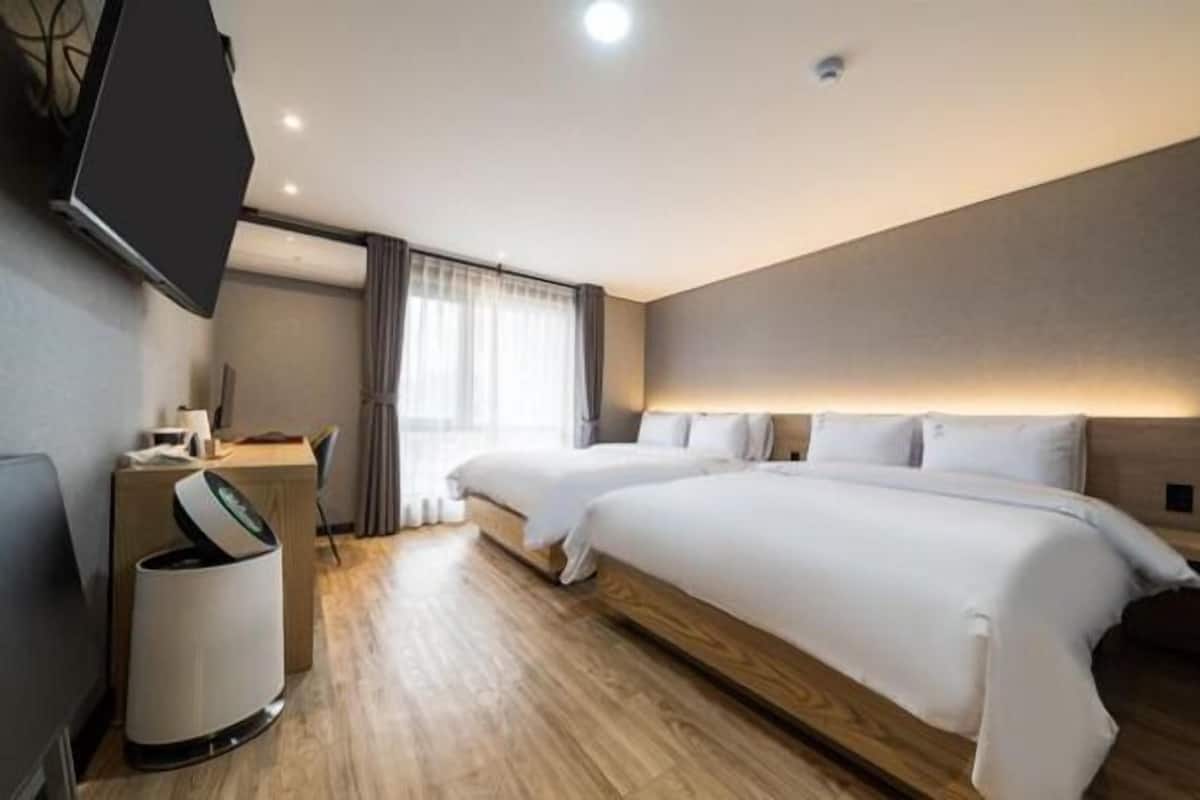 Una habitación de hotel con dos camas, un escritorio, un cesto de basura y un televisor montado en la pared.