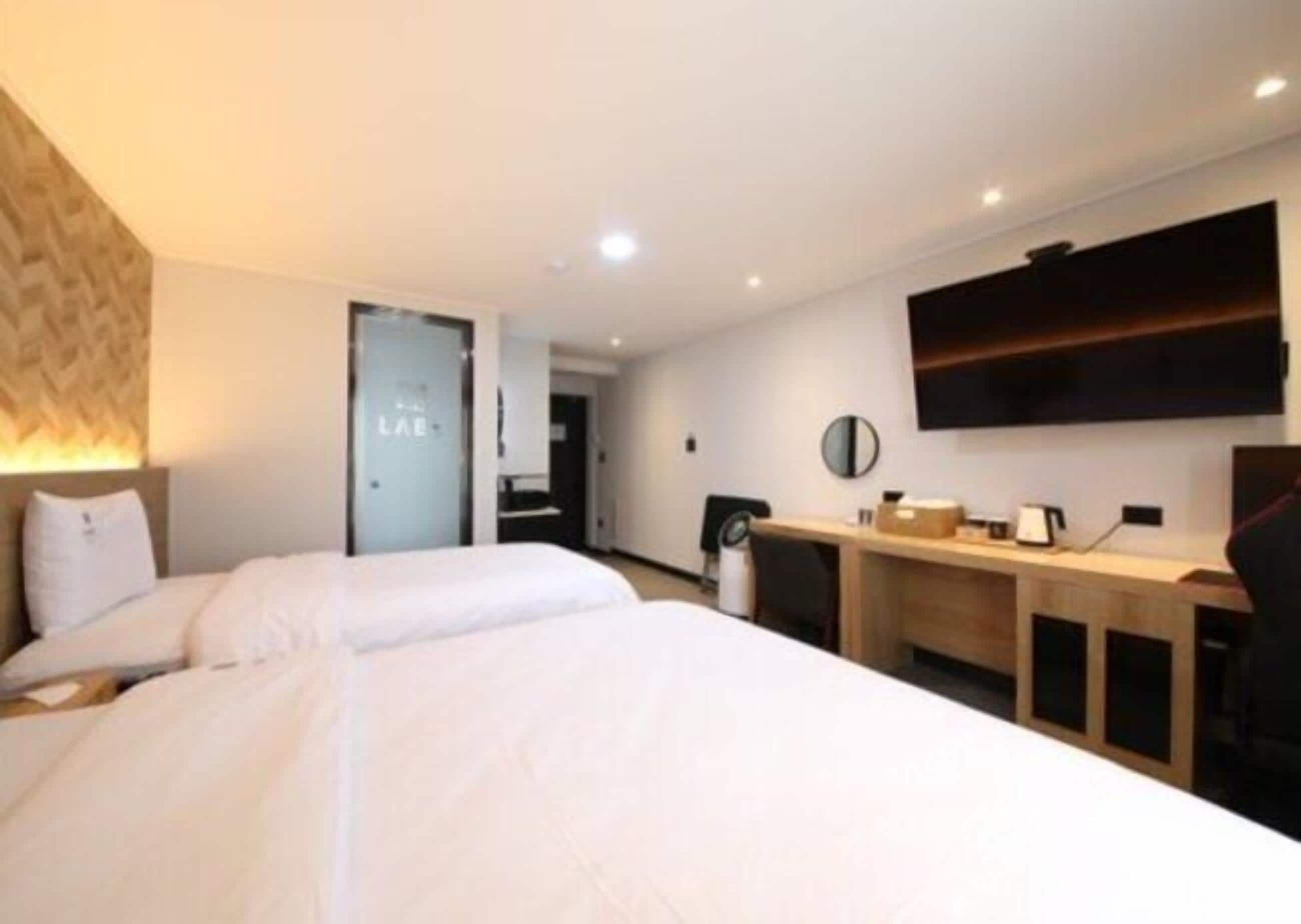 A modern hotel room with a large bed, a desk, and a flat-screen TV mounted on the wall.