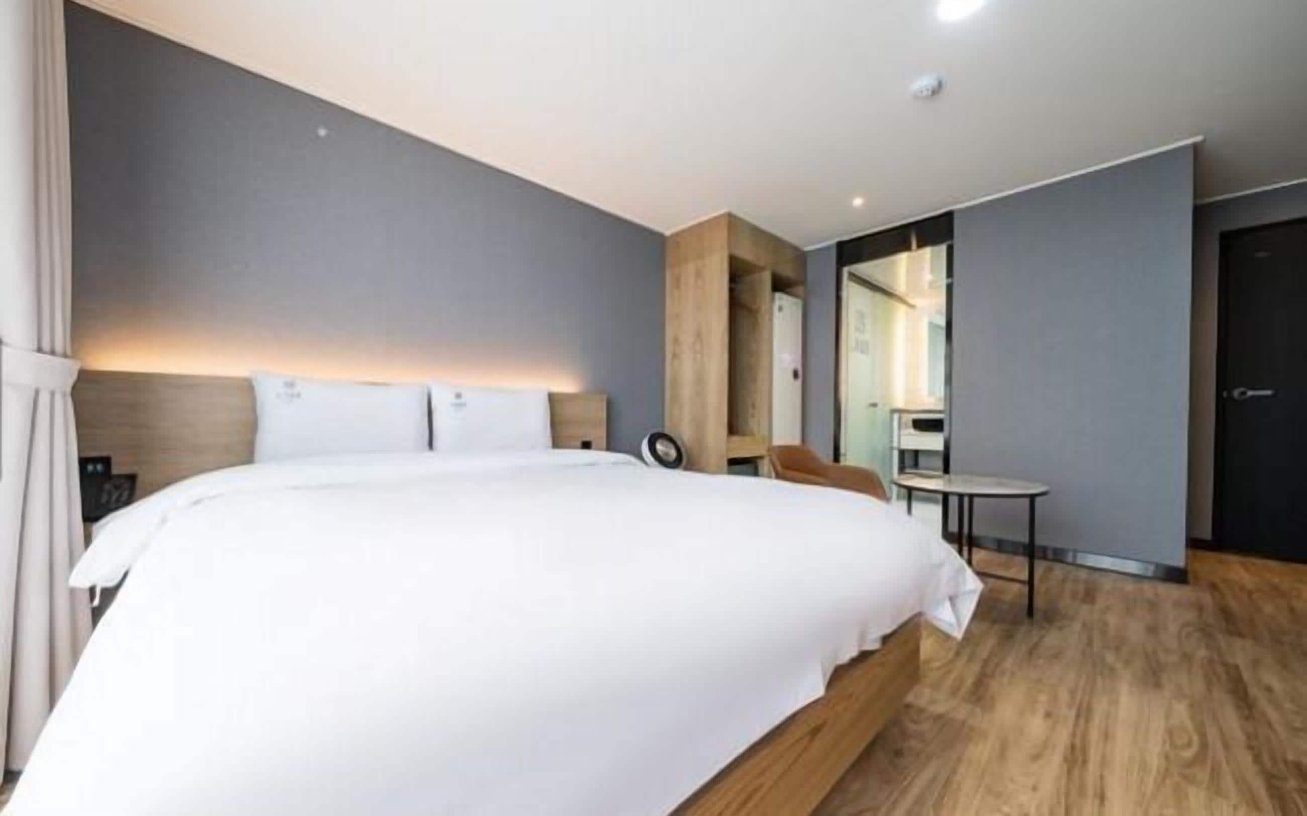 A modern hotel room with a large bed, a wooden headboard, a small table, and a mirror.