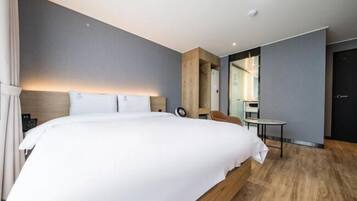 A modern hotel room with a large bed, a wooden headboard, a small table, and a mirror.