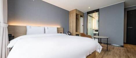 A modern hotel room with a large bed, a wooden headboard, a small table, and a mirror.